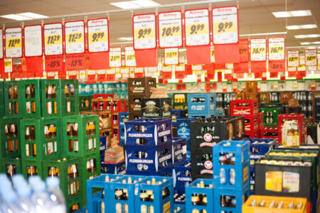 Viele gestapelte Bierkisten verschiedener Marken mit zahlreichen roten Angebots-Preisschildern im Getränkemarkt