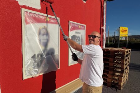 Mitarbeiter streicht die Fassade des Getränke Star Marktes in Trier mit roter Farbe während der Neugestaltung des Außenbereichs