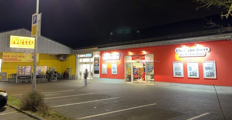 Beleuchteter Getränke Star Getränkemarkt in Trier bei Nacht mit Parkplatz vor dem Gebäude neben einem Netto-Markt