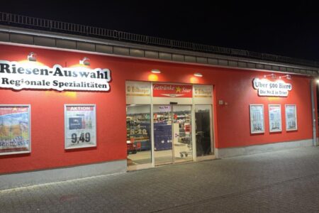 Beleuchteter Eingang des Getränke Star Getränkemarktes in Trier bei Nacht mit roter Fassade und Werbeschildern für Bierangebote