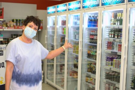 Frau zeigt auf Getränkekühlschränke mit gekühlten Getränken im Getränke Star Getränkemarkt in Trier