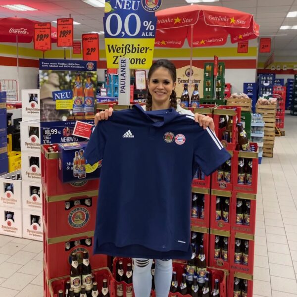 Mitarbeiterin präsentiert ein T-Shirt vor einer Paulaner Weißbier Zitrone Aktionsfläche im Getränke Star Markt in Trier