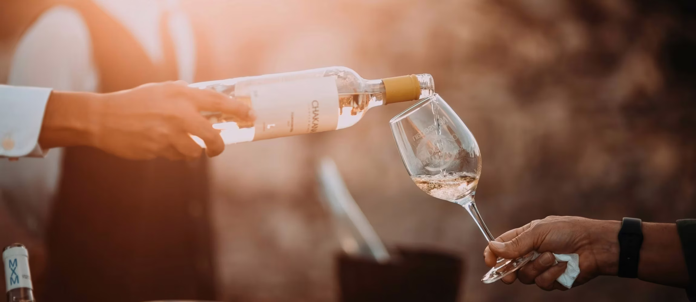 Person schenkt Weißwein aus einer Flasche in ein Weinglas